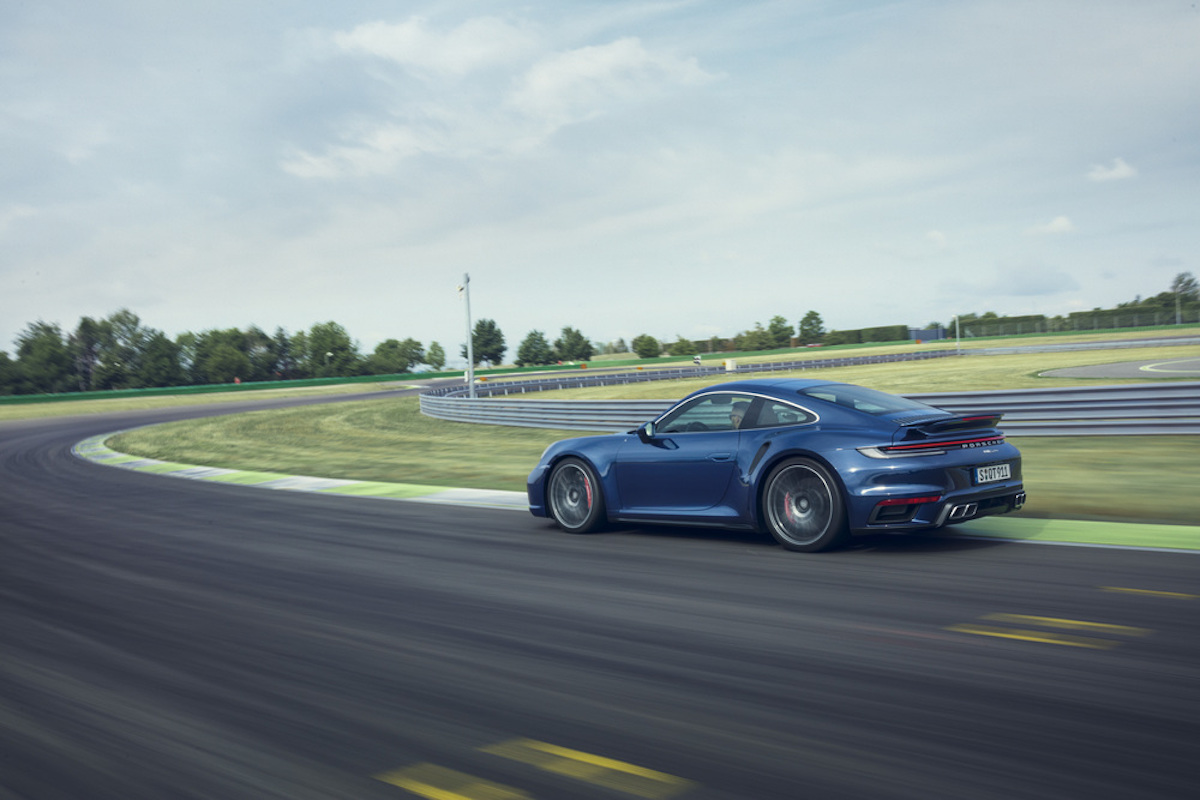 A side/back view of a navy blue Porsche Type 992 911 Turbo S trying out the twisties on a track.